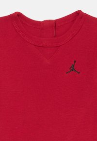 T-shirt en coton rouge avec un col rond et un logo Jumpman noir sur la poitrine gauche. Présente une texture lisse et un détail de couture en V.
