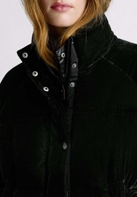 Melnas samta pūkaina jaka ar augstu apkakli, sudraba spraudņu pogām un noslēptu rāvējslēdzēju ar gludu iekšējo oderējumu.