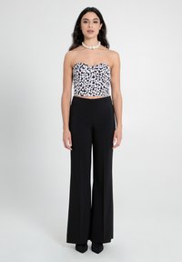 Schwarze, hoch taillierte, weite Hosen kombiniert mit einem trägerlosen Crop-Top in Schwarz und Weiß mit Punktemuster, das aus einem strukturierten Stoff gefertigt ist und einen gewellten Ausschnitt hat.