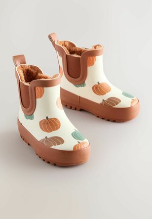 Witte rubberen laarzen met een bruine zool en afwerking, voorzien van een pompoenpatroon in oranje en groen. Gevoerd met zachte bruine vacht voor extra warmte.