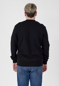 Black sweatshirt with long sleeves and round neck, paired with blue denim jeans. The fabric appears smooth, with ribbed cuffs and hem.