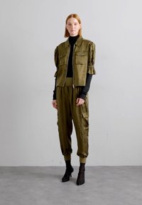 Olivovo zelený outfit pozostávajúci z krátkej bomber bundy s nastaviteľným zipsom a nadýchanými rukávmi, spolu s voľnými cargo nohavicami. Čierny rolák je pod ňou.