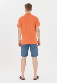Orange polo t-shirt med korta ärmar, kombinerad med ljusblå rullade shorts och mörka sandaler. Enkla design utan synliga mönster.
