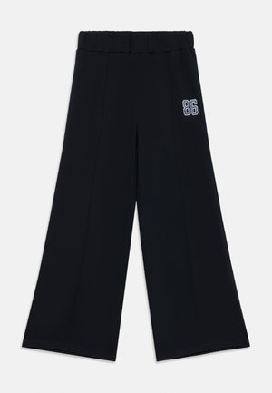 Svart vide bukser med elastisk midje, med et sydd detalj og en brodert "86" aksent på ett ben. Jevn tekstur.