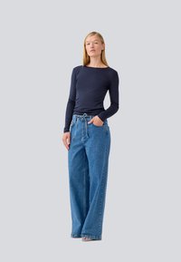 Camicia a maniche lunghe blu navy abbinata a jeans chiari a vita alta e fit rilassato, con vita elasticizzata e design a cinque tasche.