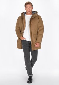 Brun hætteparka med grå foret hætte, forlommer og knaplukning. Sammenført med grå jeans og sorte støvler.