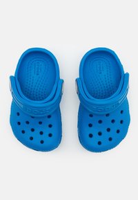 Modré Crocs vyrobené z lehkého, flexibilního materiálu; obsahují ventilační otvory, odstranitelné popruhy na patě a texturované podrážky pro lepší přilnavost.