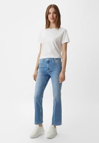 Jasnoniebieskie dżinsy o prostym kroju, zestawione z jednolitą białą bawełnianą koszulą i białymi butami sportowymi. Gładka faktura, minimalistyczny design.