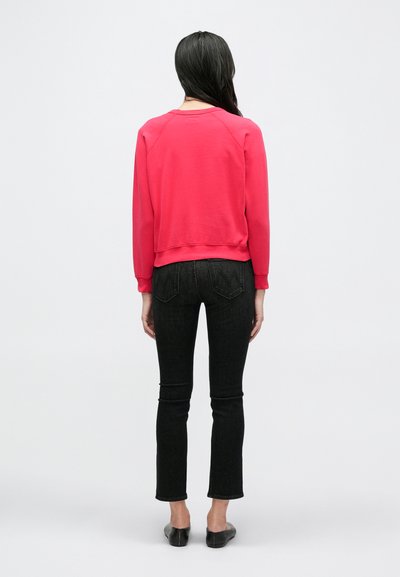 Raudonas džemperis su prigludusiu dizainu ir ribotais rankogaliais, derinamas su juodais siaurais džinsais. Lygus paviršius be raštų ar matomų logotipų.