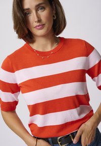 Red and white striped knit sweater with short sleeves, featuring a round neckline. Paired with a blue denim belt accentuated by a gold buckle.