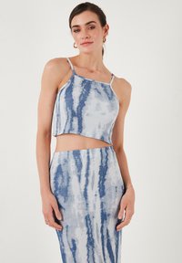 Modrý a bílý tie-dye crop top s tenkými ramínky a volným střihem, doplněný o odpovídající sukní s vysokým pasem, obě v ribované textuře.