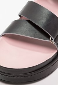 Černá kožená sandál s dvěma širokými popruhy, růžovou stélkou a hladkým povrchem. Podrobný šev podél podešve.