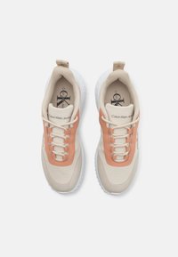 Baskets beiges avec des accents orange, en matériaux en mesh et synthétiques, bout rond, design à lacets, et une languette au talon.