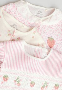 Drie babykledingstukken: een lichtroze met bloemmotief, een witte met geborduurde aardbeien en een roze gestreept ontwerp met aardbeienaccenten.