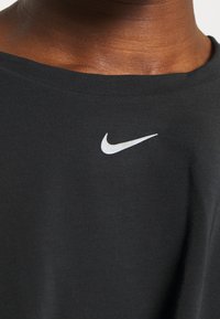 Camiseta de algodón negra con cuello redondo que presenta un pequeño logo blanco de Nike en el área del pecho izquierdo. Textura suave, diseño simple.