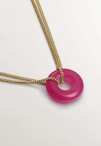 Collar de cadena en tono dorado con un gran colgante en forma de dona rosa translúcida. El colgante presenta una textura suave y una abertura circular.