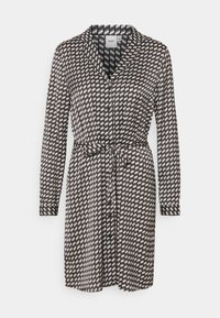 Svart och vit mönstrad klänning med långa ärmar, knäppning fram, krage och justerbart midjeband. Har diagonala linjer och geometriska former.