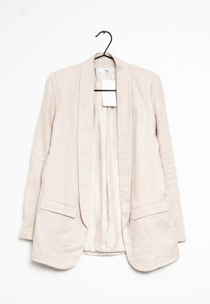 Blazer in lino beige chiaro con apertura frontale, due tasche anteriori e una fodera interna liscia, appeso a un gancio nero su uno sfondo bianco.
