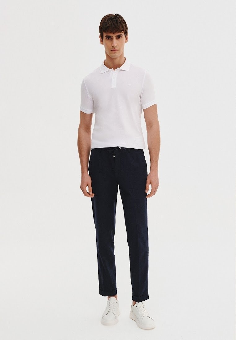 Biała koszulka polo, granatowe spodnie i białe sneakersy na męskim modelu. Koszulka ma kołnierz; spodnie są zwężane i mają elastyczny pas.