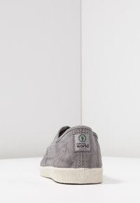 Scarpa slip-on in tela grigia con tomaia texture, suola in gomma bianca e etichetta verde "natural world" sul tallone. Design minimalista.