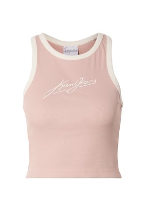 Jonge vrouw met lang blond haar, die een roze cropped top en zwarte shorts draagt, staand tegen een effen lichte achtergrond, glimlachend.
