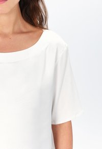 Top bianco a maniche corte realizzato in tessuto liscio. Presenta un ampio scollo rotondo e un design delle spalle senza cuciture. Estetica pulita e minimalista.