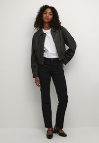 Gemaffine donkergrijze leren jas met een puntige kraag, een wit T-shirt eronder en slim fit zwarte broek. Zwarte ballerina's maken de look compleet.