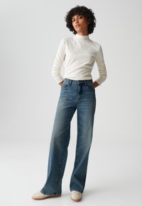 Cream long-sleeve top with a mock neck; high-waisted, blue wide-leg jeans; light sneakers with a textured design.
