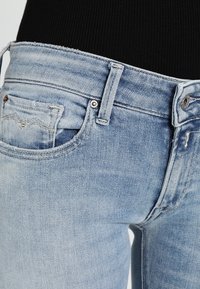 Jasnoniebieskie dżinsy z frontową kieszenią i szlufkami na pasek, noszone z czarnym topem prążkowanym.