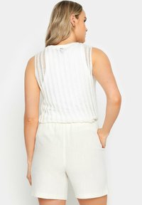 Witte gebreide tanktop met verticale doorzichtige strepen, gecombineerd met lichtbeige shorts. De top heeft een gegolfde zoom en een aansluitende taille.