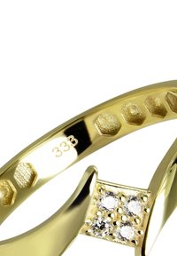 Bague en or avec une finition polie, présentant des motifs hexagonaux sur l'anneau et quatre pierres claires incrustées dans un petit sertissage. Gravée "333."