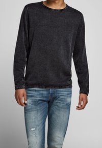 Chemise noire à manches longues avec col rond, en tissu doux. Associée à un jean denim bleu délavé avec un effet usé.