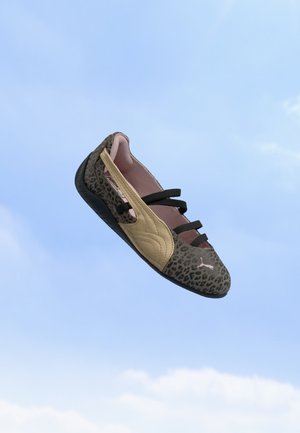 Chausson sportif avec imprimé léopard, détail latéral beige, sangles noires et le logo Puma flottant sur un ciel bleu clair.