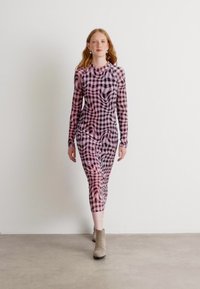 Langdurige, aansluitende jurk in een roze en zwart geruit patroon met een golvende textuur. Middenkuitlengte, gecombineerd met enkellaarsjes.