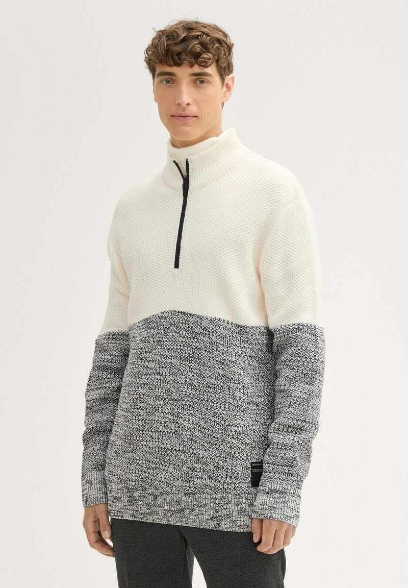 Pull à moitié zippé texturé en crème et gris. Comprend des motifs de tricot variés, des poignets côtelés et un détail de zip contrasté.