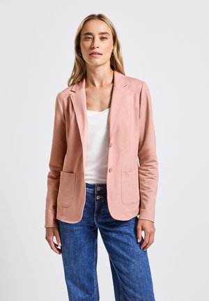 Blazer rosa chiaro realizzato in tessuto morbido, con revers a punta, due tasche frontali e una vestibilità su misura, abbinato a jeans blu.