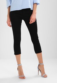 Pantalones cortos negros de mezclilla con un diseño ajustado, combinados con sandalias de tacón alto de color azul claro. Textura suave, estilo minimalista.