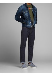 Jeansjacka i mörkblått med kontrastsömmar, grön t-shirt med logotyp, mörka jeans och grå mockaskor. Avslappnat outfit uppvisad.