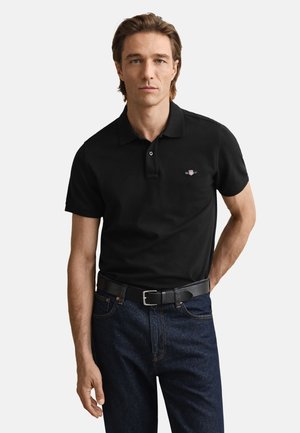Black polo shirt with a collar and two buttons, paired with dark denim jeans and a black belt. Features a small logo on the chest.