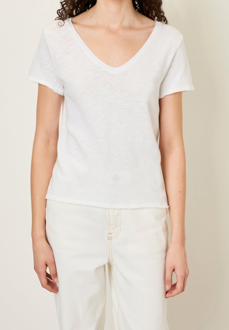 Wit katoenen V-hals T-shirt met korte mouwen, voorzien van een licht ongelijke zoom en een zachte, gestructureerde afwerking. Gecombineerd met beige jeans.