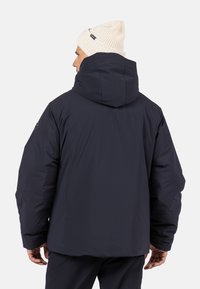 Námorně modrá puffa bunda s kapucí, vyznačující se silnou izolací, hladkým povrchem a rovnými liniemi. Nositelná s krémovou pletenou čepicí.