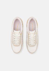 White sneakers with beige accents, lace-up design, textured panels, and gold hardware details. Branding visible on the tongue and sides.