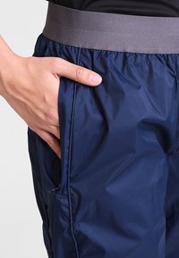 Dunkelblaue, leichte Hose mit glatter Textur, ausgestattet mit einem grauen elastischen Bund und seitlichen Taschen.