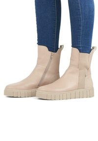 Botas de tobillo beige hechas de cuero suave, con paneles laterales elásticos, una cremallera lateral y una suela de goma gruesa y texturizada.