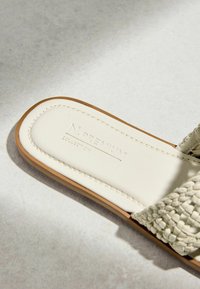 Gros plan d’une sandale à bride tissée crème avec une semelle couleur tabac et une semelle intérieure cousue embossée "N.PREMIUM COLLECTION."