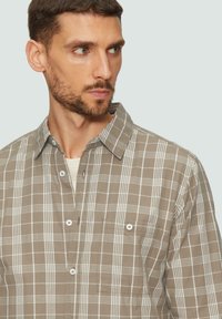 Chemise à carreaux marron et blanc en coton, avec un col rabattu, une poche poitrine et une fermeture à boutons, offrant une texture douce.