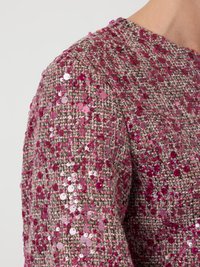 Detailný pohľad na ružovú a béžovú tkaninu tweed s hustým rozmiestnením lesklých ružových flitrov na ramene a hornej časti rukáva odevu.