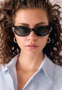 Kaķa acs saulesbrilles ar bruņurupuča rakstu un tumšām lēcām, diviem sudraba akcentiem pie sānu kājiņām, valkātas kopā ar gaismazilu svītrainu kreklu.