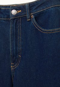 Tmavomodré rifle z denimu s klasickým strihom, žltým prešitím, kovovým zapínaním na gombík a detailmi predných vreciek.