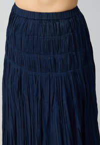 Gonna plissettata blu navy con vita elasticizzata, caratterizzata da una texture verticale e un orlo irregolare che aggiunge interesse visivo.